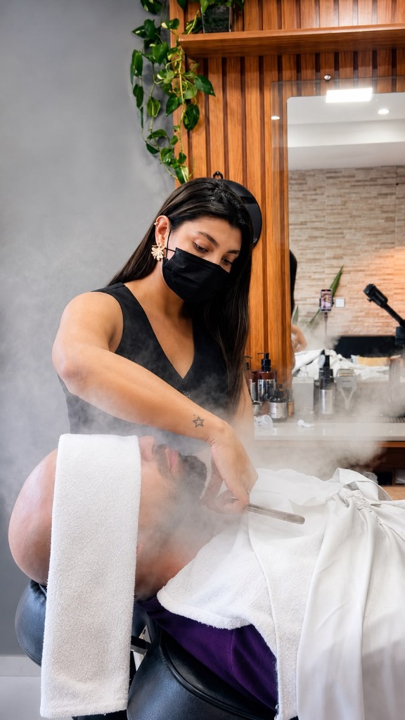 Jéssica, especialista da Patrona Barbearia, realizando um barbear de precisão com toalha quente e vaporizador